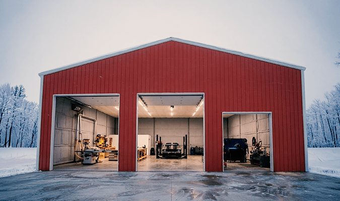 An enclosed steel workshop building with two roll-up doors and a walk-in side door